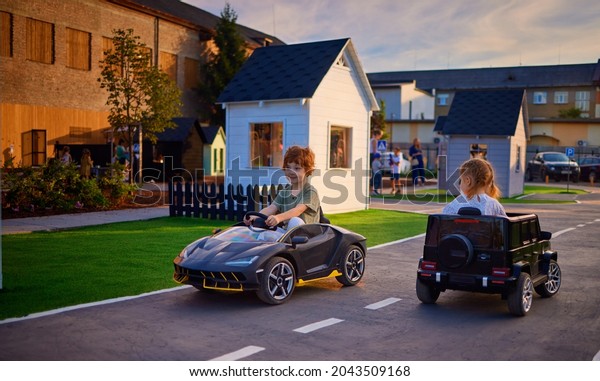 happy kids are driving the electric toy\
cars, moving around the toy city at the\
playground