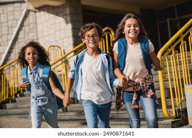 Happy kids elementary school pupils children with rucksacks backpack walking holding hands at school yard running out outside at the end of the lessons. Finish school and summer vacation concept. - Powered by Shutterstock