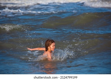 Happy Kids Have Fun In Sea On Beach. Blue Ocean With White Big Wawes On The Background. Kid Swimming In Sea With Wawes.