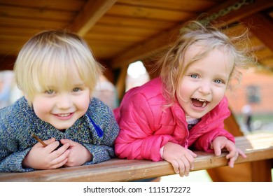 Happy Kids Having Fun On Outdoor Playground. Spring/summer/autumn Active Sport Leisure For Children. Portrait Of Little Boy And Girl Playing On Kindergarten Backyard