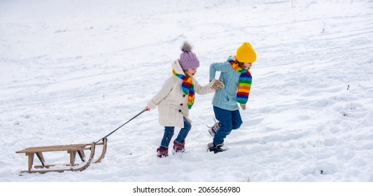 Happy kids having fun and riding the sledge in the winter snowy forest. Winter Christmas holidays and active winter weekend, children activities. Snow background, banner copy space.
