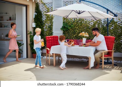 Happy Kids Helping Mother To Lay Up The Table At The Summer Patio, Family Lifestyle