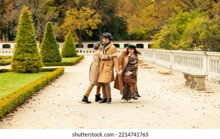Happy Kids Jump On Parents In Autumn Park. Having Fun Walking Outdoor Together, Enjoying Time At Weekend, Wear Warm Clothes.Stylish Cheerful Family. Fall Season. Parenthood,childhood Horizontal Plane.