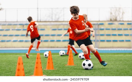 Happy Kids on Training Soccer Drill. Football Summer Camp. Young European Footballers Dribbling Around Cones in Drill. Soccer Boys in Red Uniforms in Training With School Young Coach - Powered by Shutterstock