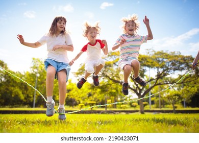 Happy Kids Play Outdoor. Children Skipping Rope In Sunny Garden. Summer Holiday Fun. Group Of School Children Playing In Park Playground. Healthy Outdoors Activity. Sport For Child.