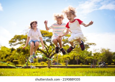 Happy Kids Play Outdoor. Children Skipping Rope In Sunny Garden. Summer Holiday Fun. Group Of School Children Playing In Park Playground. Healthy Outdoors Activity. Sport For Child.