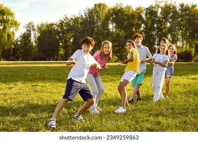 Happy kids playing games and having fun in summer camp on vacation. Team of children playing tug of war, standing on green field and pulling rope all together. Summer, fun, activity, teamwork concept - Powered by Shutterstock