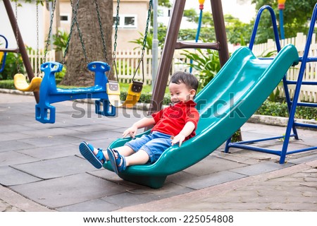 Happy kids playing on slide. Lovely school aged asian child on the chute