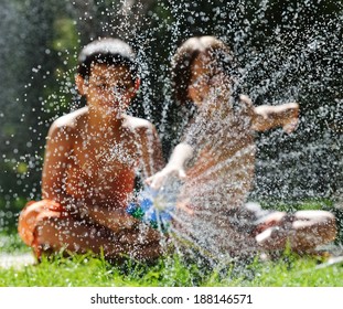 Happy Kids Playing And Splashing With Water Sprinkler On Summer Grass Yard