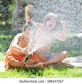 Happy Kids Playing And Splashing With Water Sprinkler On Summer Grass Yard