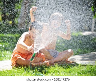 Happy Kids Playing And Splashing With Water Sprinkler On Summer Grass Yard