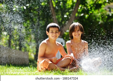 Happy Kids Playing And Splashing With Water Sprinkler On Summer Grass Yard