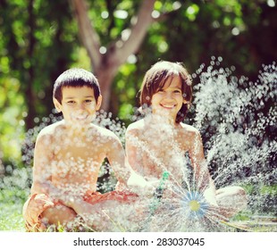 Happy Kids Playing And Splashing With Water Sprinkler On Summer Grass Yard