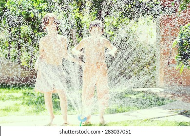 Happy Kids Playing And Splashing With Water Sprinkler On Summer Grass Yard