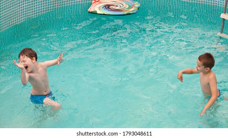 Happy Kids Playing In The Swimming Pool With Ball And Water Mattress. Having Fun In Water Pool Outside On Summer Day. Leisure And Swimming At Holidays. Happiness And Joy.