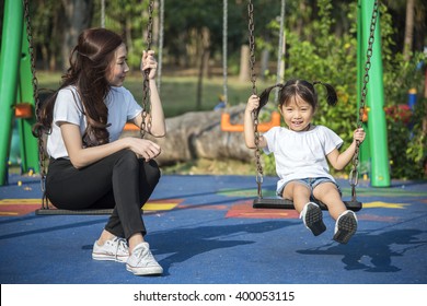 Happy Kids Playing A Swing With Her Mother In A Park