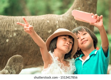 Happy Kids Playing And Take Photo By Smartphone, Family Children Holding Mobilephone And Smiling, Asain Child Sitting On Deer Statue In Zoo And Learning Outdoors On Summer Holiday 