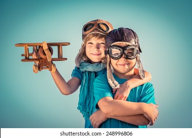 Happy Kids Playing With Vintage Wooden Airplane Outdoors. Portrait Of Children Against Summer Sky Background. Travel And Freedom Concept. Retro Toned