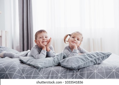 Happy kids playing in white bedroom. Little boy and girl, brother and sister play on the bed wearing pajamas. Family at home