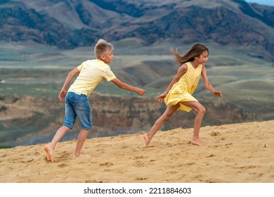 Happy Kids Run After Each Other In The Sand Dunes While On Holiday At Mountainside.