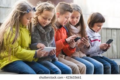 Fröhliche Kinder, die auf der Bank sitzen mit mobilen Geräten auf der Straße