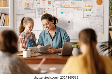 Happy kids and teacher at school. Woman and children are talking in the class. - Powered by Shutterstock