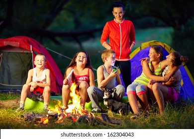 happy kids telling interesting stories around campfire