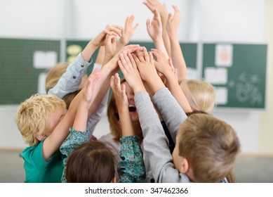 Happy Kids And Their Female Teacher Putting Their Hands Up Together Inside The Classroom.