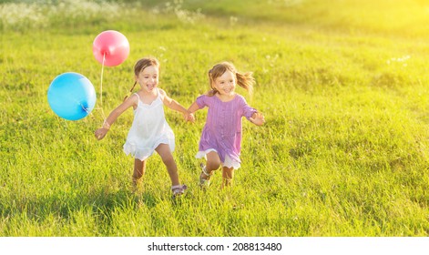 Happy Kids Twin Sisters Running Around Laughing And Playing With Balloons In The Meadow In Summer