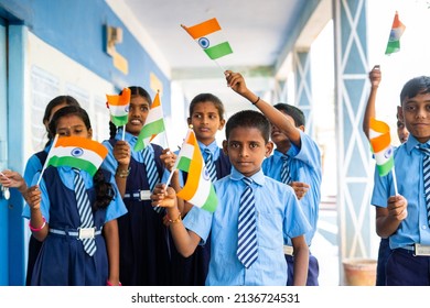 Happy kids in uniform waving indian flag by looking camera at school corridor - concept of independence or republic day celebration, patriotism and freedom.
