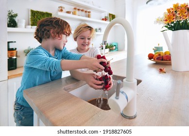 happy kids washing cherries under the tap water at the kitchen. focus on cherries