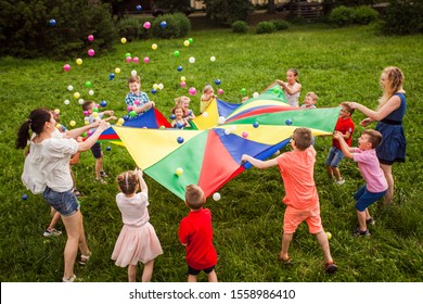 Happy kids waving rainbow parachute full of balls - Powered by Shutterstock