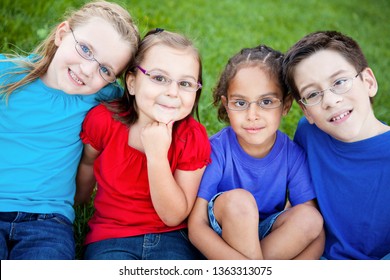 Happy Kids Wearing Glasses Sitting Together In Grass Outside - Portrait