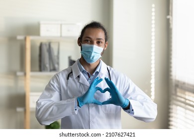 Happy Kind Young African American General Practitioner Doctor In Protective Facemask And Disposable Gloves Showing Love Sign With Hands, Giving Psychological Support And Care To Ill Patients.