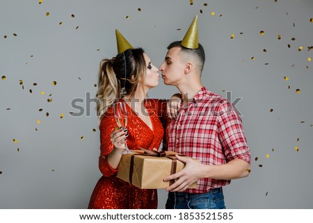 Happy kissing couple celebrating new year holding present over gray background