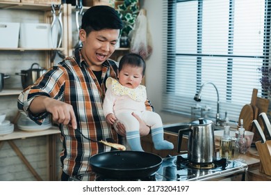 happy Korean father carrying his innocent baby girl in arm is using a spatula to fry food by the kitchen stove during daytime at home. - Powered by Shutterstock