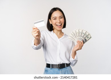 Happy Korean Woman Holding Credit Card And Money Dollars, Smiling And Laughing, Posing Against White Studio Background