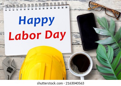 Happy Labor Day Concept.Top View With Safety Helmet, Smartphone,glasses,cup Of Coffee And Green Leave On Wood Table Background. Business And Industry Idea.