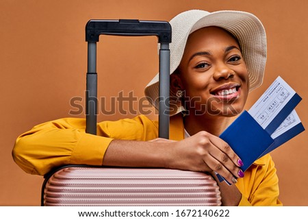 Happy lady with earrings with luggage looks at the camera and holds tickets