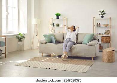 Happy lady leaning back on comfy sofa in cozy bright living room in her own apartment. Relaxed woman enjoying free time on quiet weekend or day off and sitting hands behind head on soft couch at home - Powered by Shutterstock