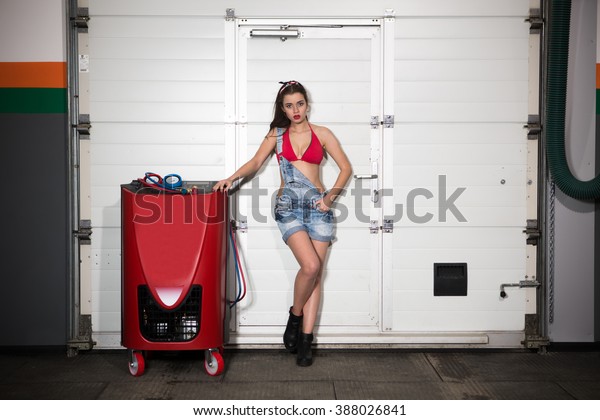 Happy lady posing near\
professional air conditioning stations for cars over white\
background in repair shop. Happy smiling woman in jeans shorts and\
red underwear.
