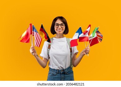 Happy lady showing bunch of diverse flags cheerfully smiling at camera over yellow studio background, excited female student recommending foreign language studying school