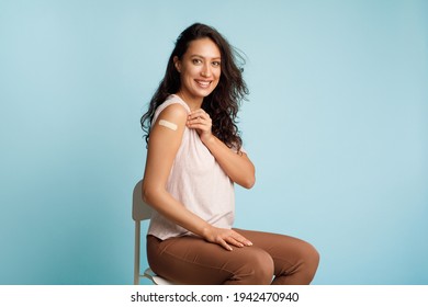 Happy Lady Showing Vaccinated Arm With Adhesive Bandage, Blue Background - Powered by Shutterstock