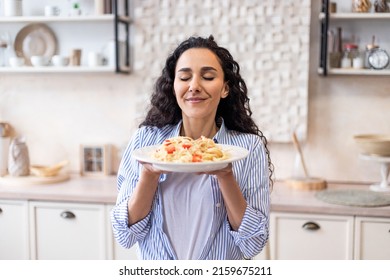 Happy lady tasting homemade spaghetti while having lunch, enjoying the smell with eyes closed, sitting in kitchen interior. Woman cooking and eating tasty food at home - Shutterstock ID 2159675211