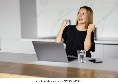 Happy Laptop User Woman Celebrating Good News, Success, Luck With Winner Yes Hands, Shouting For Joy At Laptop In Home Kitchen, Laughing, Feeling Excited, Surprise, Winning Prize