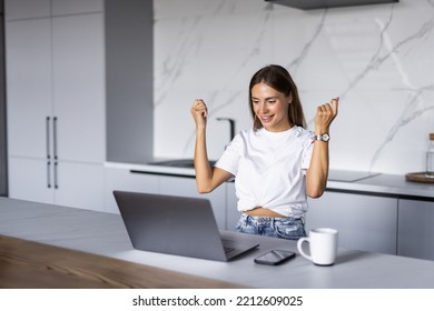 Happy Laptop User Woman Celebrating Good News, Success, Luck With Winner Yes Hands, Shouting For Joy At Laptop In Home Kitchen, Laughing, Feeling Excited, Surprise, Winning Prize