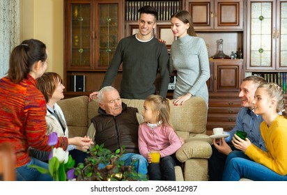 Happy Large Family Gathered In Parental Home For Family Party, Cheerfully Talking In Cozy Living Room