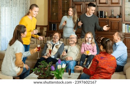 Happy large family gathered in parental home for family party, cheerfully talking in cozy living room
