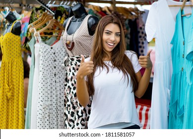 Happy Latin American Woman Presenting Clothes At Market Outdoor In Summer In City