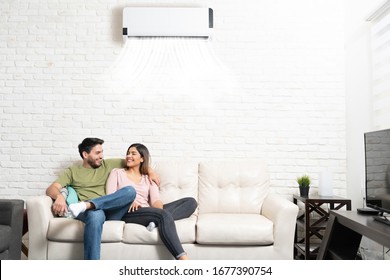 Happy Latin boyfriend and girlfriend relaxing on sofa in living room at home with air conditioning